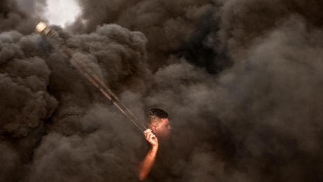 A Palestinian protester uses a slingshot in front of Israeli forces as smoke rises from burning tyres during a protest near the border with Israel, east of Gaza City. (Mahmud Hams / AFP) A Palestinian protester uses a slingshot in front of Israeli forces as smoke rises from burning tyres during a protest near the border with Israel, east of Gaza City. (Mahmud Hams / AFP)