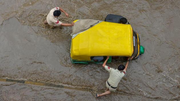 Policemen try to move an auto-rickshaw that broke down on a flooded street following heavy rainfall, in Gurugram, Haryana. (PTI) Policemen try to move an auto-rickshaw that broke down on a flooded street following heavy rainfall, in Gurugram, Haryana. (PTI)