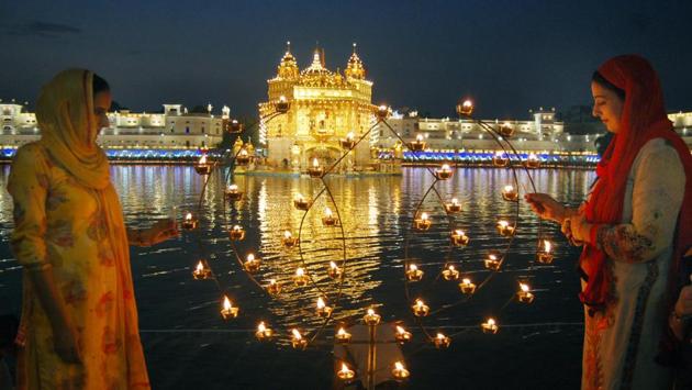 Devotees lighting lamps with the Golden Temple in the backdrop on Monday. (sameer sehgal/ht)