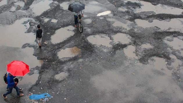 Commuters walks past potholes at Bandra station bus stop. Prakash Bilhore was travelling pillion when the motorbike he was on with his cousin hit a deep pothole, sending them both flying through the air. Prakash, who wasn’t wearing a helmet, suffered fatal brain damage. The tragic accident occurred during Mumbai’s summer monsoon when heavy rains are blamed for causing crater-like holes. (Prabhat Mehrotra / HT File)