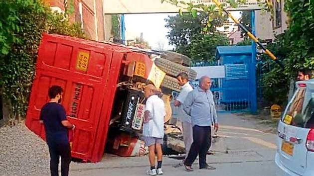 Residents said they were jolted by a loud noise, as the truck, laden with construction material, overturned at a curve after a wheel on its rear left side slipped into a stormwater drain.(HT Photo)