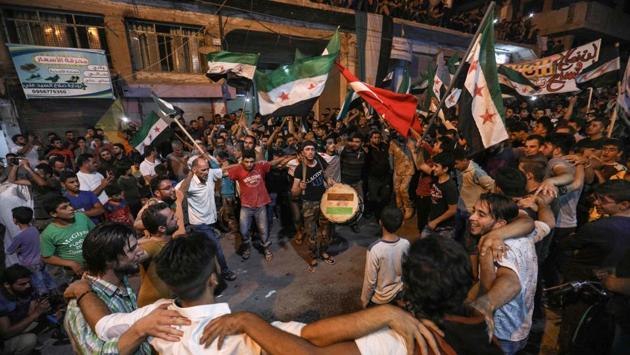 Syrians dance, chant slogans and strike drums while others wave flags of Turkey and the opposition, as they protest against the Syrian government during a demonstration in Binnish in the rebel-held northern Idlib province. (Omar Haj Kardour / AFP)