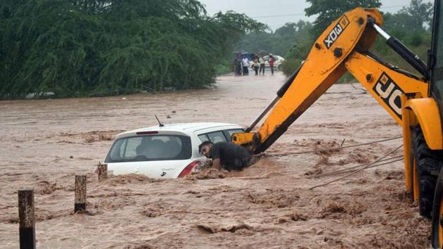 A JCB machine lifting a car that got stuck in an overflowing rivulet near Dadumajra in Chandigarh on Monday.(HT Photo)