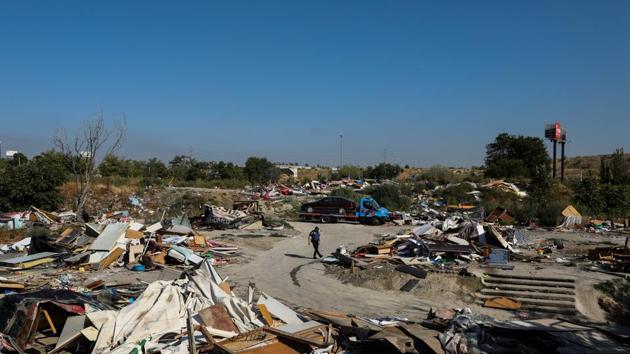 A police officer walks amid debris as a truck tows an abandoned car during the demolition drive. “Mum cried when we left the camp,” said Beatriz, one of nine children at the flat, as volunteers helped set out their furniture.  (Susana Vera / REUTERS) 