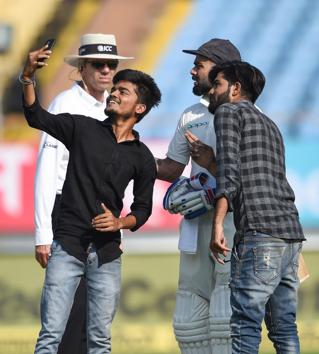 Rajkot: Indian batsman Virat Kohli interacts with his fans who forced their way into the field to take a selfie with the player during the ongoing test cricket match played between India and West Indies in Rajkot (PTI) Rajkot: Indian batsman Virat Kohli interacts with his fans who forced their way into the field to take a selfie with the player during the ongoing test cricket match played between India and West Indies in Rajkot (PTI)