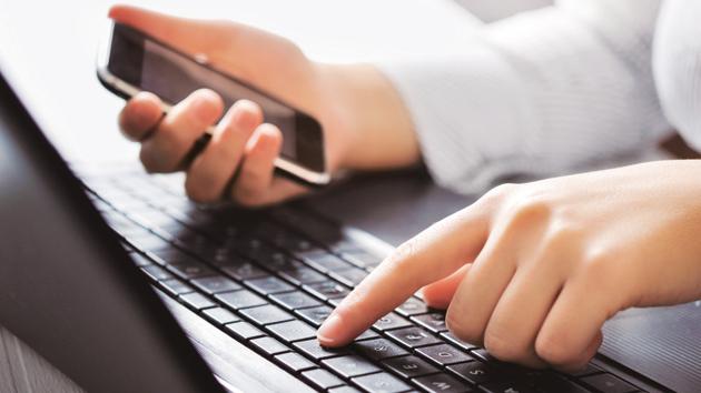 A person using laptop keyboard and holding a mobile phone.(Getty Images/iStockphoto)
