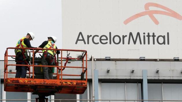 Workers stand near the logo of ArcelorMittal, the world's largest producer of steel, at the steel plant in Ghent, Belgium.(Reuters File Photo)