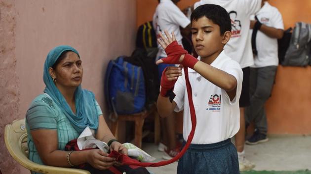 A young boxer puts on hand wraps before a training session. Rohit Shokeen, a boxing coach at Najafgarh stadium, said that children there are more focused on sports than studies and parents support them. Most youngsters want to get into the armed forces, and sports only enhance their chances. (Vipin Kumar / HT Photo) 