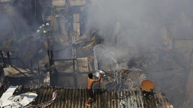 A boy pours water trying to douse a fire at a slum in Mumbai. Two children were injured and nearly 70 houses were gutted in a fire that broke out at around 11.30 am and was brought under control by 1 pm. A senior fire department official said that 7-8 gas cylinder blasts led to the massive blaze. (Rafiq Maqbool / AP)