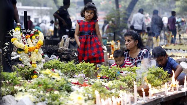 A family sits around the grave of their loved one after decorating it with candles and flowers. Christians follow the annual observance by offering flowers and lighting candles on the graves of their departed loved ones on All Souls Day at the St Sepulclchers cemetery in Pune,on Friday. (Rahul Raut/HT PHOTO) 