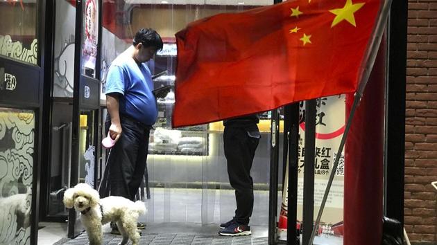 A man walks his dog as he leaves a restaurant flying the Chinese national flag in Beijing, China.(AP Photo)