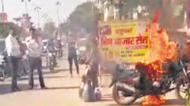 Traffic policemen (left) look on as the accused (centre) unties milk containers from the burning motorcycle (right) on Tuesday afternoon near DSD College on New Railway Road, Gurugram. (HT Photo) Traffic policemen (left) look on as the accused (centre) unties milk containers from the burning motorcycle (right) on Tuesday afternoon near DSD College on New Railway Road, Gurugram. (HT Photo)