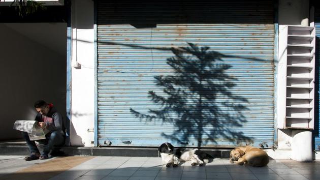 A man reads a newspaper as stray dogs sleep next to a closed shop in Dharmsala, Himachal Pradesh. (Ashwini Bhatia / AP) A man reads a newspaper as stray dogs sleep next to a closed shop in Dharmsala, Himachal Pradesh. (Ashwini Bhatia / AP)