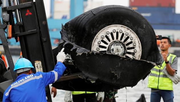 A worker assists his colleague during the lift up of a damaged tyre from Indonesian forensic policemen stand beside a damaged tyre from the the Lion Air flight JT610 jet.(REUTERS)