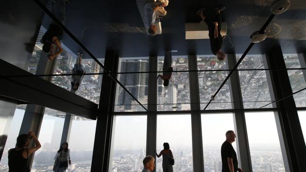 Tourists are reflected in ceiling mirrors as they view the Bangkok cityscape during a visit of the King Power Mahanakhon building Bangkok, Thailand. (Sakchai Lalit / AP) Tourists are reflected in ceiling mirrors as they view the Bangkok cityscape during a visit of the King Power Mahanakhon building Bangkok, Thailand. (Sakchai Lalit / AP)