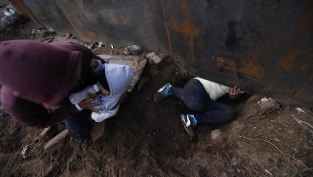 Honduran migrant Joel Mendez, 22, feeds his eight-month-old son Daniel as his partner Yesenia Martinez, 24, crawls through a hole in the rain-softened soil under the wall, in Tijuana, Mexico. Moments later Martinez surrendered to waiting border guards while Mendez stayed behind in Tijuana to work, saying he feared he’d be deported if he crossed. (Rebecca Blackwell / AP) Honduran migrant Joel Mendez, 22, feeds his eight-month-old son Daniel as his partner Yesenia Martinez, 24, crawls through a hole in the rain-softened soil under the wall, in Tijuana, Mexico. Moments later Martinez surrendered to waiting border guards while Mendez stayed behind in Tijuana to work, saying he feared he’d be deported if he crossed. (Rebecca Blackwell / AP)