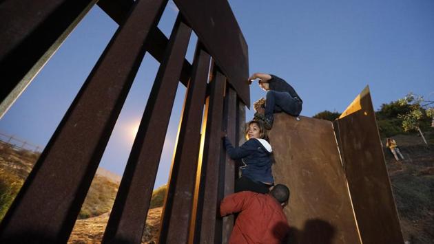 A group of young people hoisted themselves over the wall to San Ysidro, California, hoping that their ticket to a better life was finally within reach. One migrant offered a hand to help the others jumping down onto US territory. (Rebecca Blackwell / AP) A group of young people hoisted themselves over the wall to San Ysidro, California, hoping that their ticket to a better life was finally within reach. One migrant offered a hand to help the others jumping down onto US territory. (Rebecca Blackwell / AP)
