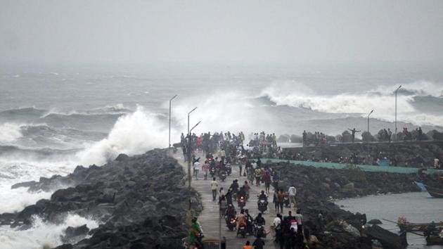 People walk along a breakwater at Kasimedu fishing harbour as Cyclone Phethai approaches Chennai on Sunday.(AFP Photo)