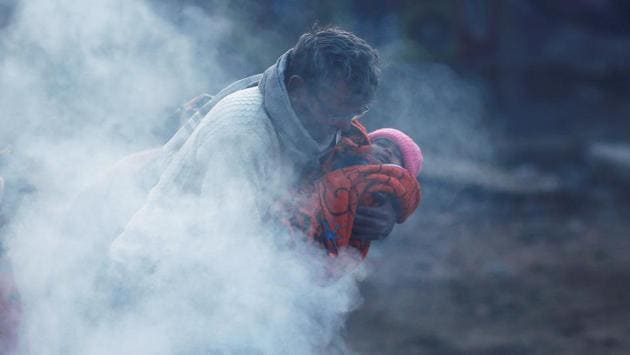 A man holding a baby wrapped in a blanket stands next to a bonfire on a cold winter morning in New Delhi. (Adnan Abidi / REUTERS)