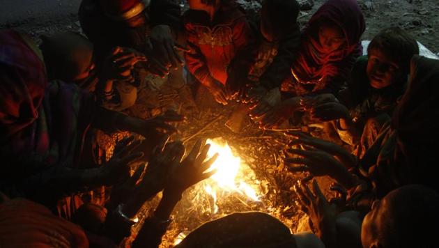 People sit near a bonfire to keep themselves warm on a cold winter evening, near Old Jail complex, in Gurugram(Yogendra Kumar/HT PHOTO)