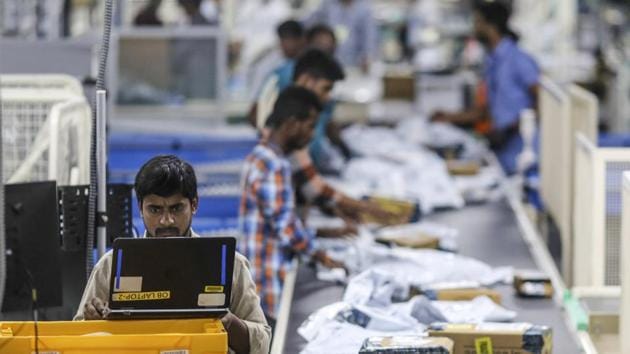 An employee uses a laptop computer while packages move along a conveyor belt at the Amazon.com Inc. fulfillment center in Hyderabad.(Bloomberg)
