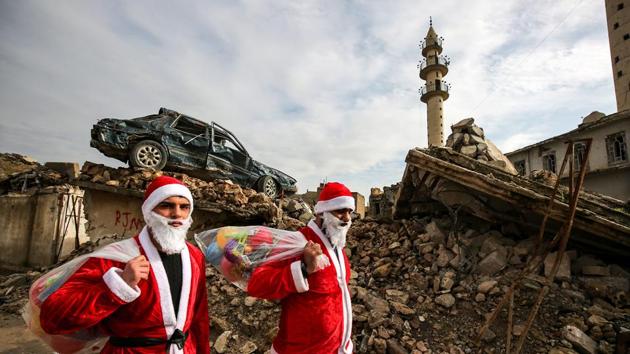 Iraqi youths dressed in Father Christmas suits walk through the streets of the old city of Mosul as they distribute gifts. (Ahmad Al-rubaye / AFP) Iraqi youths dressed in Father Christmas suits walk through the streets of the old city of Mosul as they distribute gifts. (Ahmad Al-rubaye / AFP)