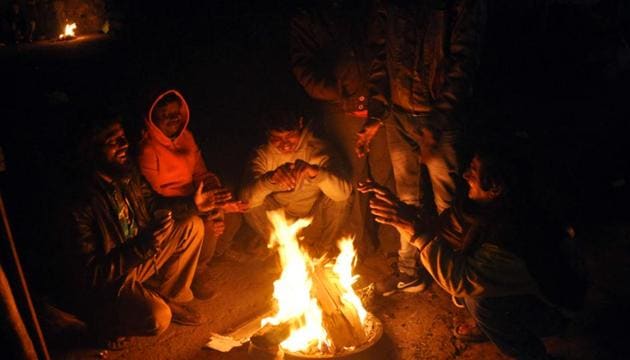 People keep themselves warm around a fire during a cold winter early morning near Mori Gate in New Delhi.(HT Photo)