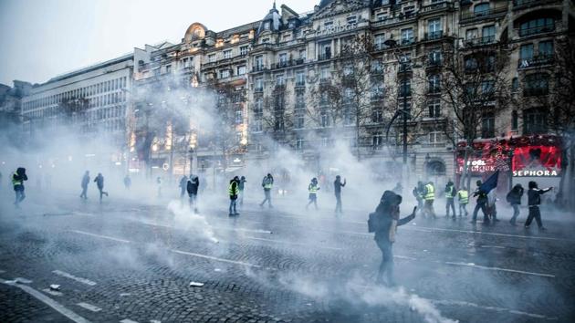 Protesters wearing yellow vests (gilets jaunes) stand amid smoke of tear gas during a demonstration against rising costs of living they blame on high taxes on the Champs-Elysees avenue in Paris, on December 15, 2018.(AFP)