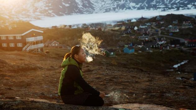 A young girl sits on a stone and smokes in the late evening sunshine above Tasiilaq. Moeller also cited another temporary advantage climate change has brought to his tourism business: People want to see the ice cap before it is too late. “Go and see the glaciers before they disappear. That’s the thing you hear again and again,” he said. (Lucas Jackson / REUTERS) A young girl sits on a stone and smokes in the late evening sunshine above Tasiilaq. Moeller also cited another temporary advantage climate change has brought to his tourism business: People want to see the ice cap before it is too late. “Go and see the glaciers before they disappear. That’s the thing you hear again and again,” he said. (Lucas Jackson / REUTERS)