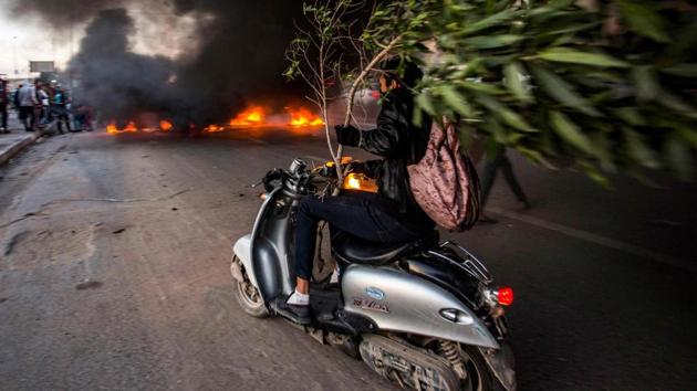 An Iraqi protester holds a broken tree as he drives a scooter towards other protesters blocking the road with a tire fire, during a demonstration against corruption and lack of services in the southern city of Basra. (Hussein Faleh / AFP) An Iraqi protester holds a broken tree as he drives a scooter towards other protesters blocking the road with a tire fire, during a demonstration against corruption and lack of services in the southern city of Basra. (Hussein Faleh / AFP)