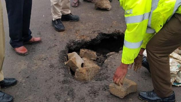 A traffic police constable seen putting bricks inside a caved in portion of a road, at Sohna road, in Gurugram, on Wednesday, January 23, 2019.(HT Photo)