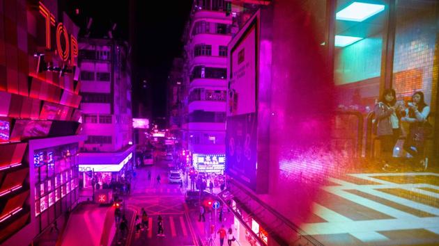A general view taken through tinted windows in a walkway between two buildings shows pedestrians on a road and a reflection of two women (R) using their phones in the walkway in Hong Kong. (Anthony Wallace / AFP)