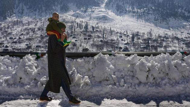 A man carrying his child, walks on a snow covered pavement as normal life is gradually returning after heavy snowfall in the Valley, at Gund area of Ganderbal district of Central Kashmir. (S Irfan / PTI)