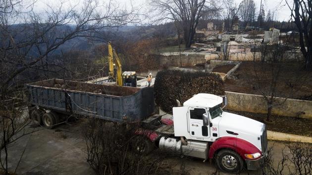 An excavator loads debris onto a truck while clearing a property burned by the Camp Fire in Paradise. Workers have been cutting down trees and clearing the burned-out lots at the town as part of the process to rebuild the town. (Noah Berger / AP Photo)