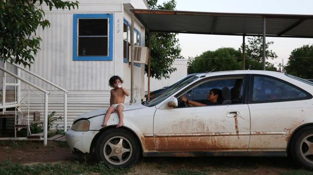 Bayron pretends to drive his neighbour's parked car as his cousin Dalila sits on the hood near the trailer where Bayron and his family temporarily lived in Texico. In San Antonio’s bus terminal, the family and other caravan members said emotional goodbyes as they took buses to different parts of the United States. They have been in Texico since May, living on trailer sites where their cousins and extended family were already. (Loren Elliott / REUTERS)