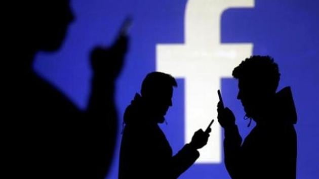 Silhouettes of mobile users are seen next to a screen projection of Facebook logo in this picture illustration taken March 28, 2018. Image for representation.(REUTERS FILE PHOTO)
