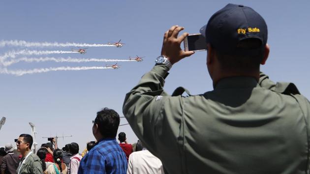 An Indian Air Force (IAF) officer films Sarang, a helicopter display team of IAF's Dhruv choppers, perform aerobatic maneuvers on the third day of Aero India 2019 at Yelahanka air base in Bangalore, India, Friday, Feb. 22, 2019. Aero India is a biennial event with flying demonstrations by stunt teams and militaries and commercial pavilions where aviation companies display their products and technology.(AP)