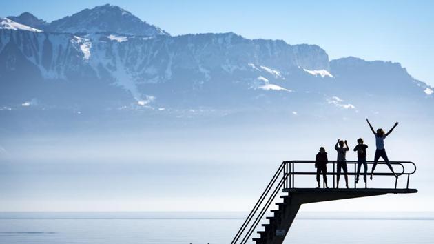 Kids enjoy the sunny and warm weather on a diving platform on the shore of the Lake Geneva in front of the Swiss and French Alps on a unusually warm winter day, in Lutry, Switzerland. (Laurent Gillieron / Keystone via AP)