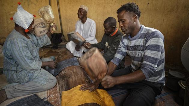 Craftsmen hammer dyed cloth with wooden mallets. The homespun cloth, hung to dry on razor wire topping the walls around the pits, ranges from sky blue to darkest night and comes in romantically named designs: moon and shadow, moon and star, three baskets (standing for wealth, education and power). (Ben Curtis / AP)