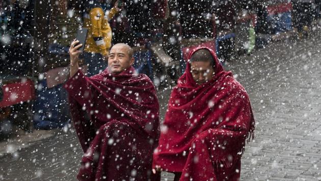 An exile Tibetan Buddhist monk uses his phone camera as he walks with another in the snow in Dharmsala, Himachal Pradesh. (Ashwini Bhatia / AP) 