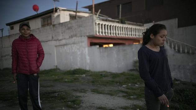 Josue Mejia Lucero (L), smokes along with his girlfriend’s sister Xiomara Henriquez Ayala, 13, outside the Agape World Mission shelter. The girls joined the caravan so they could meet their father, who had left them in Mexico’s southern border city of Tapachula in August while he tried to get to the United States. (Emilio Espejel / AP) Josue Mejia Lucero (L), smokes along with his girlfriend’s sister Xiomara Henriquez Ayala, 13, outside the Agape World Mission shelter. The girls joined the caravan so they could meet their father, who had left them in Mexico’s southern border city of Tapachula in August while he tried to get to the United States. (Emilio Espejel / AP)