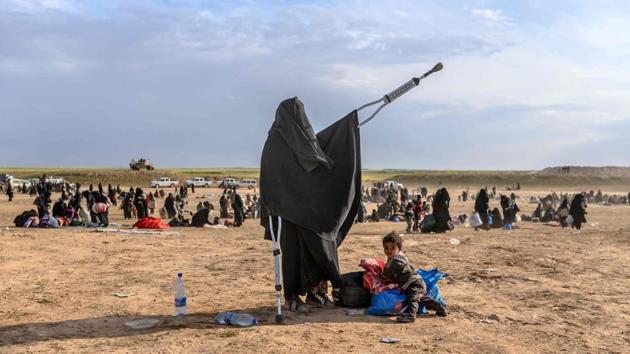 A woman walking with crutches stands next to a child as people evacuated from the Islamic State (IS) group’s embattled holdout of Baghouz arrive at a screening area held by the US-backed Kurdish-led Syrian Democratic Forces (SDF), in the eastern Syrian province of Deir Ezzor. (Bulent Kilic / AFP) 