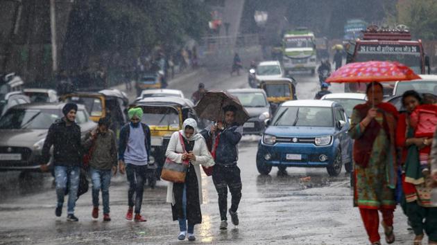 Pedestrians cross a street during rains, in Jammu. According to a news report, the temperature is likely to remain steady as another active Western Disturbance will be affecting the northern hills between March 13 and 15. (PTI)