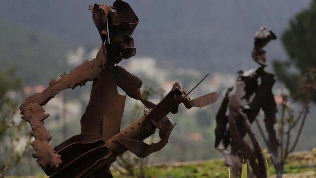 A view of a sculpture of a person strumming at a guitar made from artillery with another in the background depicting a farmer with a rake in hand and tilling his field, by Charles Nassar in his Remhala garden. (Joseph Eid / AFP) A view of a sculpture of a person strumming at a guitar made from artillery with another in the background depicting a farmer with a rake in hand and tilling his field, by Charles Nassar in his Remhala garden. (Joseph Eid / AFP)