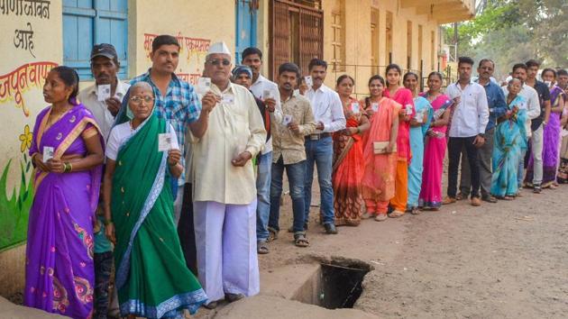 Voters show their voter cards as they stand in a queue to cast their votes.(PTI)