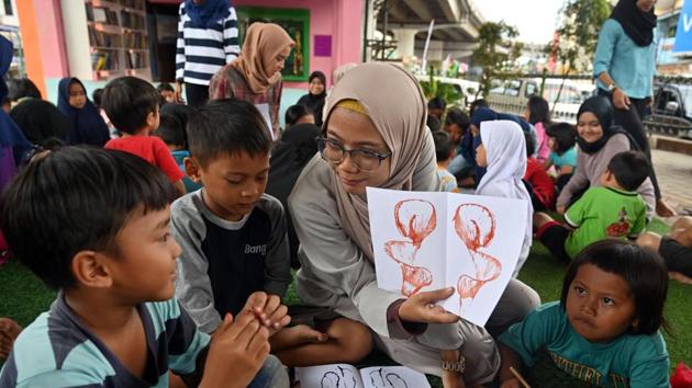 A volunteer shows art to children. Artists painted murals on the walls, installed planter boxes and a futsal pitch, and a library with several dozen books was built on site. Still, it wasn’t met with universal acclaim when it opened for business in 2016. “In the beginning not everyone was supportive when we came with books because there were already other residents here,” Febrianti said. (Adek Berry / AFP) A volunteer shows art to children. Artists painted murals on the walls, installed planter boxes and a futsal pitch, and a library with several dozen books was built on site. Still, it wasn’t met with universal acclaim when it opened for business in 2016. “In the beginning not everyone was supportive when we came with books because there were already other residents here,” Febrianti said. (Adek Berry / AFP)