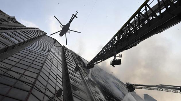 A helicopter carries water to drop on a burning office building as Bangladeshi firefighters on ladders work to extinguish the blaze in Dhaka, Bangladesh. (Munir Uz Zaman / AFP) A helicopter carries water to drop on a burning office building as Bangladeshi firefighters on ladders work to extinguish the blaze in Dhaka, Bangladesh. (Munir Uz Zaman / AFP)