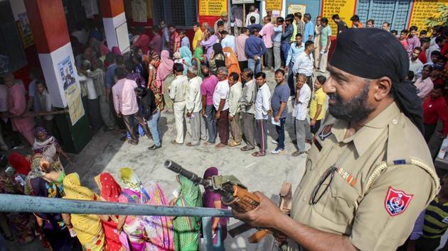 A security personnel stands guard as voters queue to cast their vote during the first phase of general elections at a polling station in Meerut on Thursday.(PTI)