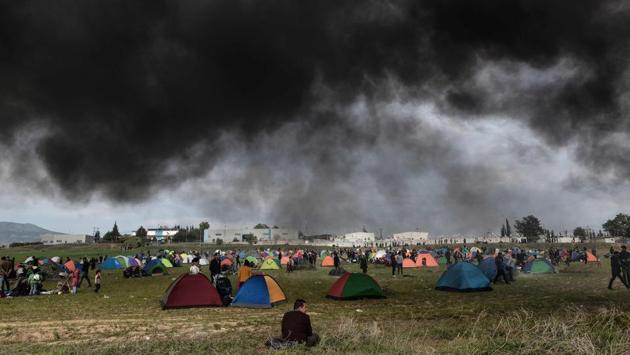 A migrant sits on the grass as smoke from a fire billows above tents outside of a refugee camp in Diavata, a western suburb of Thessaloniki, where migrants gathered in Greece. Hundreds of migrants and refugees gathered following anonymous social media calls to walk until the Northern borders of Greece to pass to Europe. (Sakis Mitrolidis / AFP) 