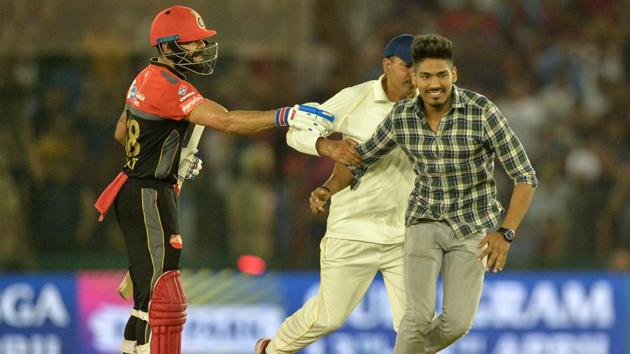 A fan (R) of Royal Challengers Bangalore (RCB) cricketer Virat Kohli (L) is pursued by a security official (C). (AFP)